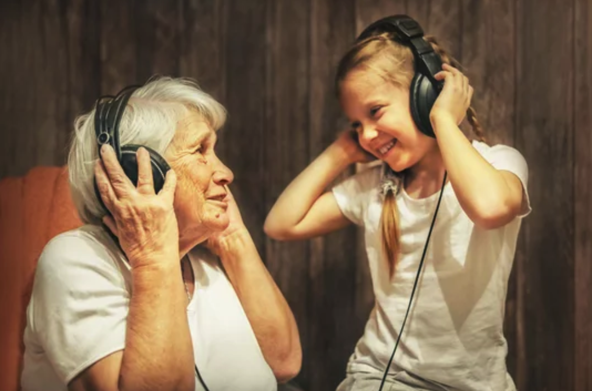 An elderly woman and a young girl smiling while listening to music with headphones.
